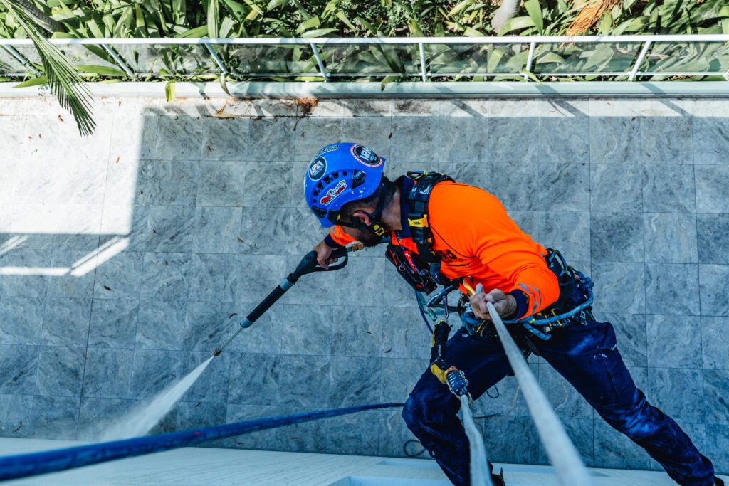 High Property Access rope access technician pressure cleaning a building wall from above